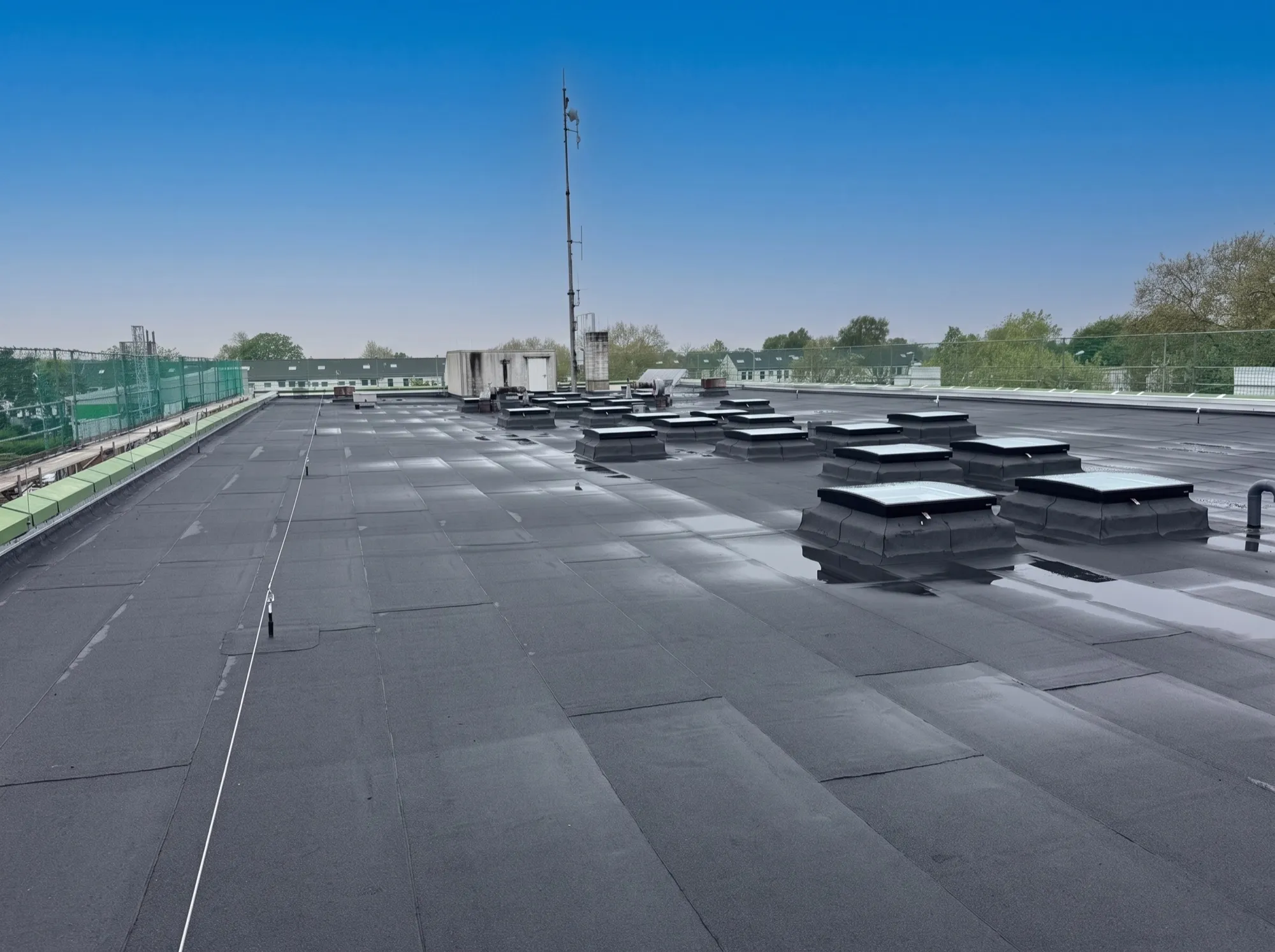 Industrie-Hallendach mit neuen Bitumenbahnen, Lichtkuppelreihen, Sicherungsseil und gepolstertem Kantenschutz im Raum Düren
