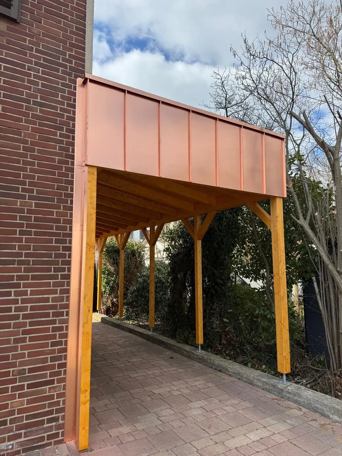 Vordach in Kupfer über einem Carport aus Holz, angeschlossen an eine Klinkerwand